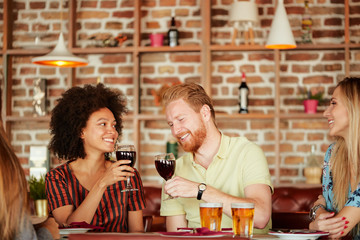 Wall Mural - Group of friends having dinner at restaurant. Friends cheering and drinking alcohol.