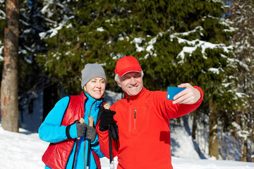 Wall Mural - Happy seniors in winter activewear making selfie on smartphone during skiing training in the forest