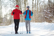 Two active seniors in sportswear trekking down forest road on frosty winter day
