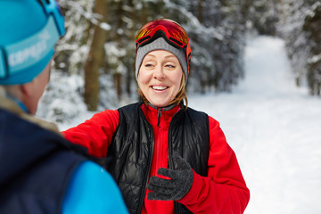 Wall Mural - Cheerful middle aged woman in sportswear talking to her husband in winter forest during training