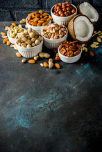 Various Types Of Nuts - Walnuts, Pecans, Peanuts, Hazelnuts, Coconut, Almonds, Cashews, In Bowls, On A Dark Blue Concrete Table Top View