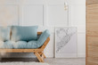 Blue sofa with pillows next to map in white frame in elegant living room interior of minimal house, real photo with copy space on the empty wall