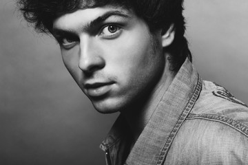 Wall Mural - Portrait of Handsome Young Man. A Men in a Denim Jacket Posing on a Gray Background. Black and White Photo