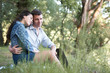 © soleg - young couple sitting on the grass in the forest and looking on sunset, summer nature, bright sunlight, shadows and green leaves, romantic feelings