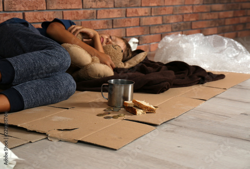 Fotografija Poor homeless boy sleeping with his toy on floor near brick wall
