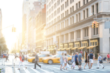 Crowds of anonymous people walking across an intersection on 5th Avenue in Manhattan New York City with colorful sunlight background