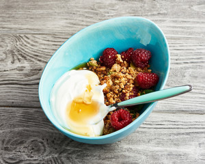 Wall Mural - Homemade granola with yogurt in a bowl with raspberries and maple syrup on a wooden table.