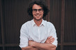 © iuricazac - Portrait of happy handsome young businessman with glasses, smiling, posing outdoors. Male student posing against brown wall. Smart guy in white shirt wears spectacles with curly hair walking on street