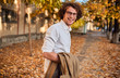 © iuricazac - Horizontal potrait of young businessman with glasses posing outdoors going to the lunch. Male student in autumn street. Smart guy in casual wears spectacles with curly hair walking down the street
