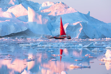 Wall Mural - little red sailboat cruising among floating icebergs in disko bay glacier during midnight sun season