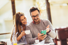 Young Cheerful Man And Woman Dating And Spending Time Together In Cafe, Using Phone.