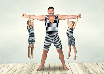 Family of strongman. The father of two sons in vintage costume of athletes perform strength exercises. Family look.