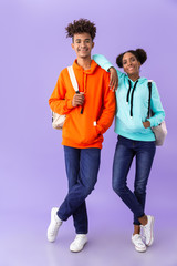 Wall Mural - Full length photo of african american students wearing backpacks hugging together, isolated over violet background