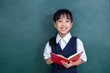 Leinwandbild Motiv Asian Chinese little Girl in uniform reading book against green blackboard