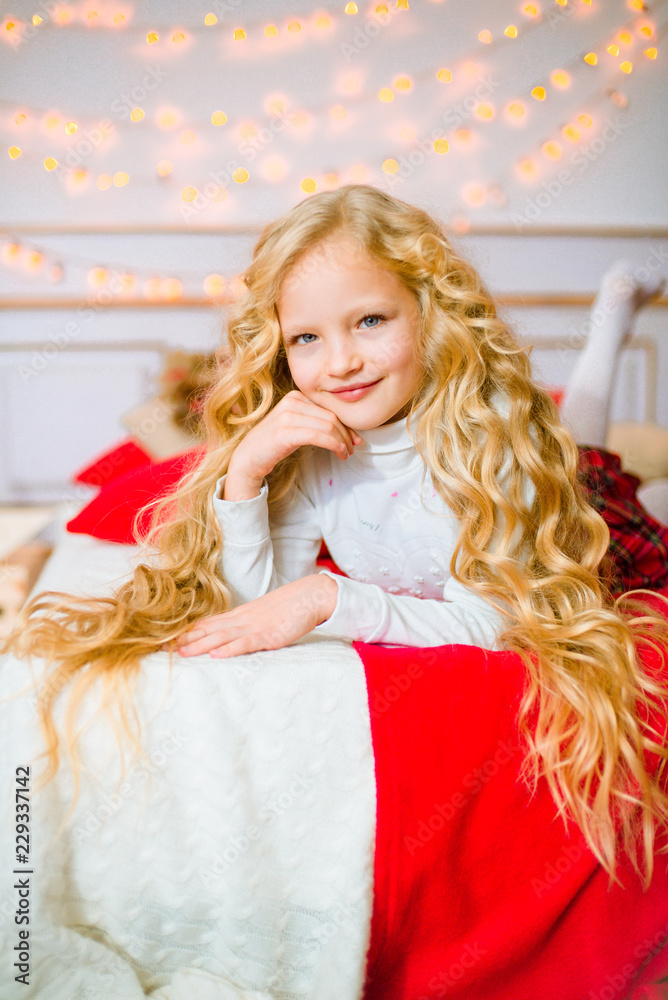 Little girl with blond long curly hair at Christmas morning.Merry Christmas.Little girl rejoices to the Christmas gift
 - obrazy, fototapety, plakaty 