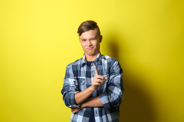 Emotional teenage boy waggling finger at viewer on color background