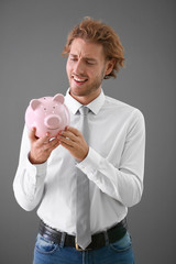 Handsome man with piggy bank on grey background