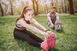 © estradaanton - Attractive girl is sitting on grass in park and stratching. She is looking straight and smiling. Her boyfriend isstretching as well and looking at her partner.