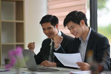 Two Asian colleagues excited goal achievement win or successful teamwork in office