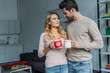 © LIGHTFIELD STUDIOS - couple clinking with cups of tea and looking at each other at home, christmas concept