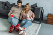 © LIGHTFIELD STUDIOS - smiling couple holding cups of cappuccino and sitting on carpet in living room