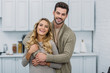 © LIGHTFIELD STUDIOS - smiling handsome boyfriend hugging attractive girlfriend in kitchen and they looking at camera