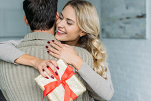 Attractive Young Woman With Gift Box Embracing Her Boyfriend At Home
