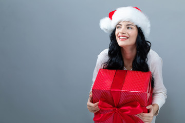 Young woman with santa hat holding a gift box on a gray background