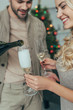 © LIGHTFIELD STUDIOS - beautiful young couple pouring champagne into glasses in front of christmas tree at home