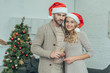 © LIGHTFIELD STUDIOS - happy young couple with champagne glasses looking at camera in front of christmas tree at home
