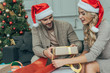 © LIGHTFIELD STUDIOS - young couple in santa hats decorating christmas gift together at home
