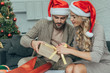 © LIGHTFIELD STUDIOS - focused young couple in santa hats decorating christmas gift together at home