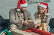 © LIGHTFIELD STUDIOS - happy young couple in santa hats decorating christmas gift together at home