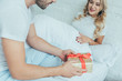 © LIGHTFIELD STUDIOS - beautiful young couple with gift sitting in bed together at home