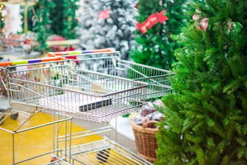 Empty shopping baskets in the shop, christmas market with green Christmas trees for sale on the background. Prepearing for Christmas eve, new year party. Selective focus. Copy space.