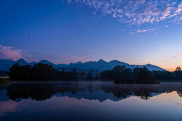 Blue hour shot of peaceful scene of beautiful autumn mountain landscape with lake, colorful trees and high peaks in High Tatras, Slovakia.