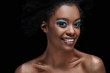 © LIGHTFIELD STUDIOS - portrait of cheerful african american model with bright blue eyes shadows isolated on black