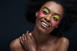 © LIGHTFIELD STUDIOS - portrait of smiling african american model with bright neon makeup posing isolated on black