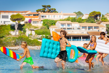 Wall Mural - Teens running into the sea with inflatable stuff