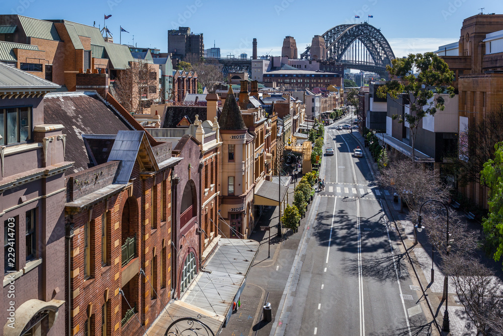 View of George Street in the Rocks, the historic district of Sydney. In the background, the harbour Bridge. - obrazy, fototapety, plakaty 