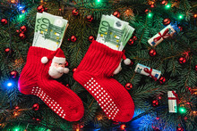 Background Of Fir Branches. Santa's Red Stockings With Money. Christmas Card. Top View. Xmas Congratulations. Lights