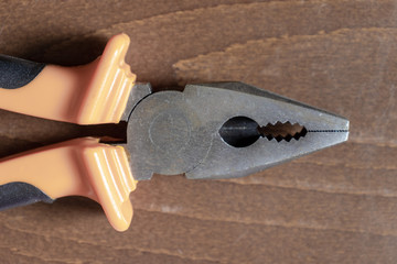 Cropped pliers with orange handles on brown wooden background