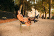 © Aleksandr - A young girl in a brown coat sits in the middle of the park on a khaki stool. Girl relax and have good day