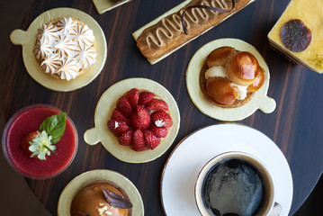 Wall Mural - Breakfast time with cup of hot coffee and pieces of cream cake with strawberries and raspberries, sweets dessert breakfast snacks, close-up. Berry cupcakes dessert on wooden table background, top view