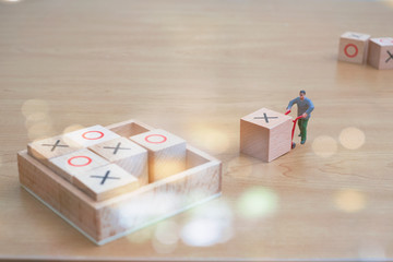 MINIATURE DELIVERY MAN WITH  X WOODEN CUBE ON HIS DOLLY TRYING TO WIN TIC TAC TOE. (PLACING 3 OF HIS MARKS IN A HORIZONTAL VERTICAL OR DIAGONAL ROW WILL WIN THE GAME)  PATIENT AND WORK HARD CONCEPT