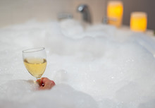 Woman Holding A Glass Of Wine In Bubble Bath With Candles