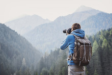 Young Cheerful Man Photographer Taking Photographs With Digital Camera In A Mountains. Travel And Active Lifestyle Concept