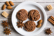 © Nataliia - Chocolate crumble cookies, decorations of cane sugar, cinnamon sticks, almonds and anise stars on grey wooden table background.