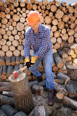 Wall Mural - Ax in hand. Man holding an industrial ax. A strong man holds an ax in his hands against the background of firewood. Strong man lumberjack with an ax in his hand.