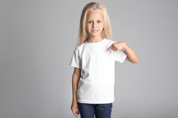 Wall Mural - Cute little girl pointing at her t-shirt on grey background